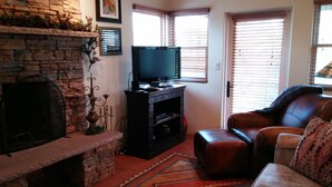 A living room with a stone fireplace, a television on a wooden stand, a leather sofa, and a patterned rug. - SANTA FE ADOBE JEWEL (Santa Fe)