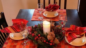 A dining table set with red and beige placemats, clear glassware, and a centerpiece with pinecones, berries, and a candle. - SANTA FE ADOBE JEWEL (Santa Fe)