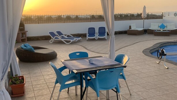 Eine Dachterrasse mit Pool, blauen Liegestühlen, einem Tisch mit Stühlen und Topfpflanzen.