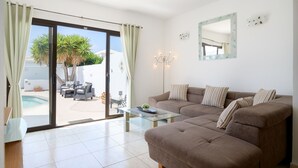 Ein modernes Wohnzimmer mit braunem Sofa, Glastisch und einer Schiebetür zu einer Terrasse mit Pool und Möbeln.