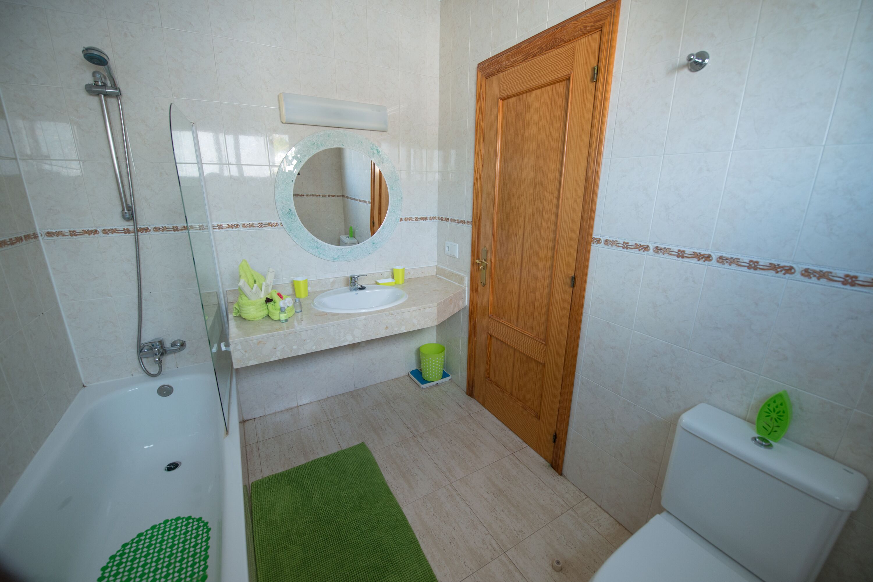 A bathroom with a bathtub, sink, mirror, toilet, and green rug.
