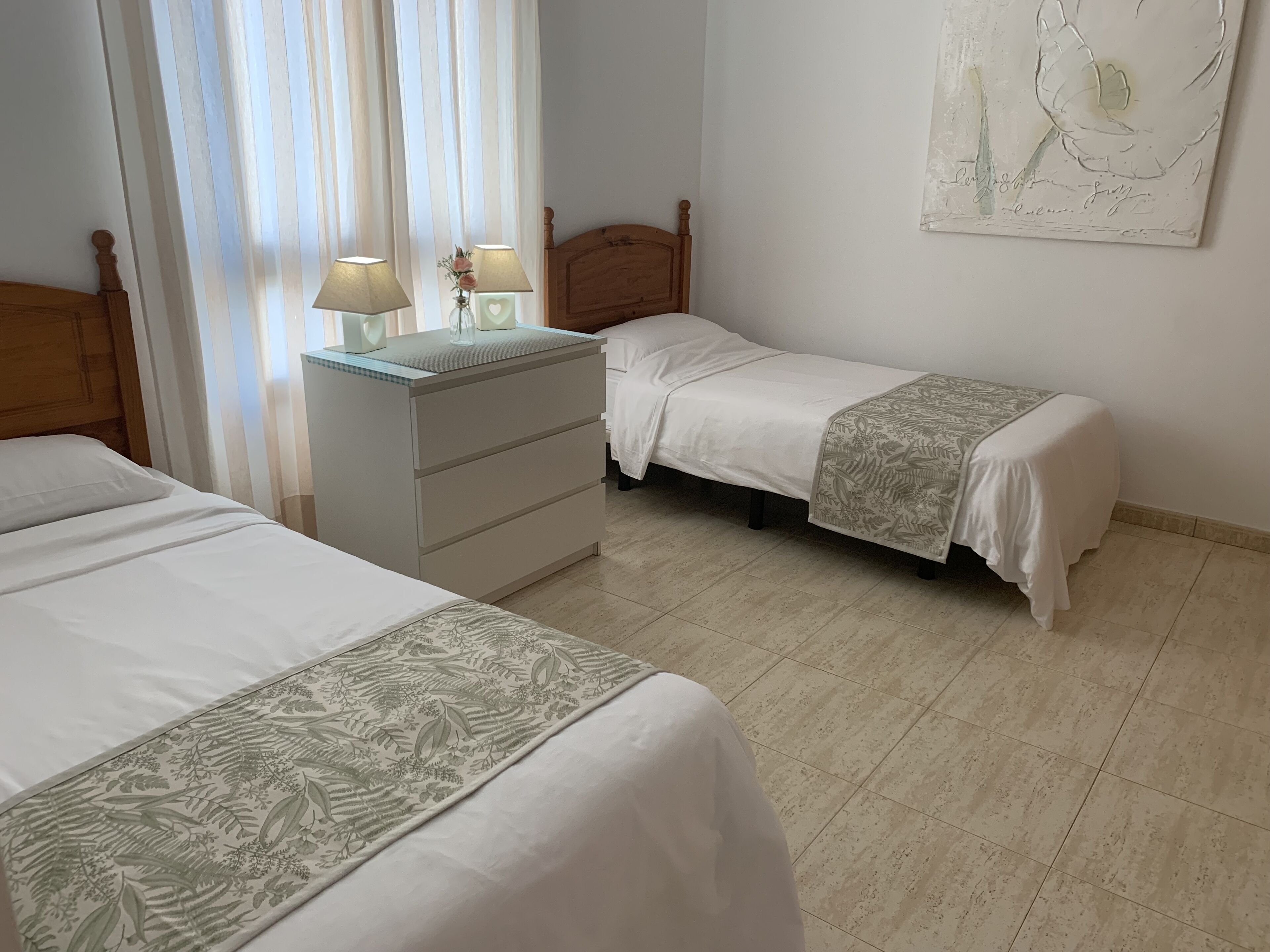 A bedroom with two beds, a nightstand, a dresser, and a wall-mounted lamp.