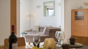 Ein modernes Wohnzimmer mit einer Couch, einem Esstisch mit Tellern, Gläsern und einer Flasche.