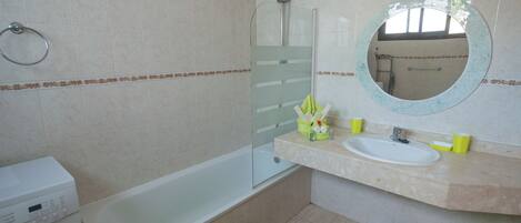 A bathroom with a bathtub, a sink, a mirror, and a washing machine.