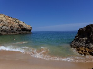 A beach with clear water, a swimmer, and rocky cliffs.