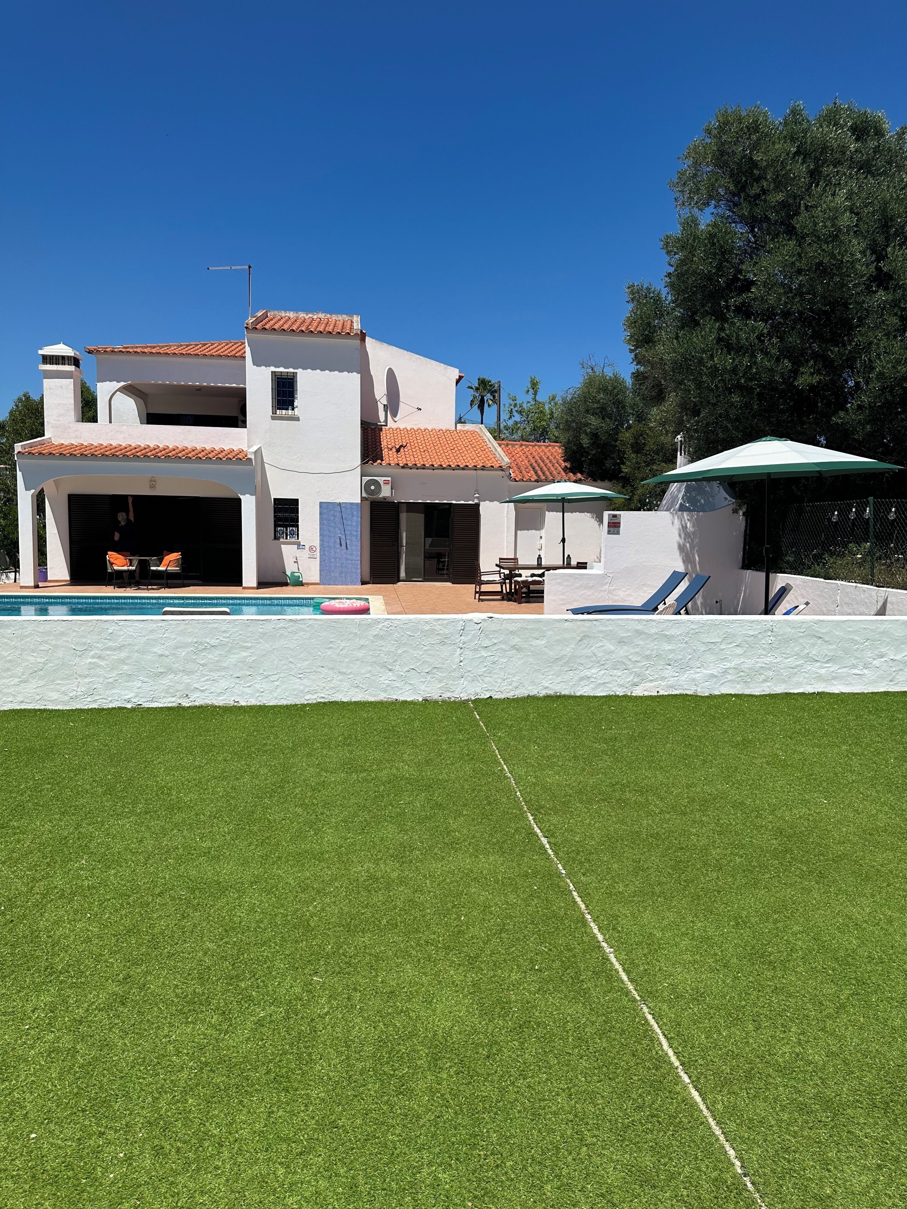 A two-story house with a swimming pool, outdoor furniture, and a satellite dish.