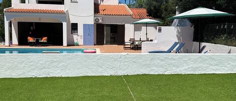 A two-story house with a swimming pool, outdoor furniture, and a satellite dish.