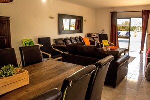 Uma sala de estar moderna com um sofá de couro marrom escuro, uma mesa de jantar de madeira e uma cadeira verde.