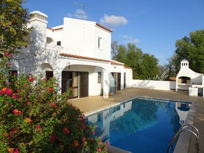 Uma vila branca com piscina, rodeada por vegetação exuberante e plantas floridas.