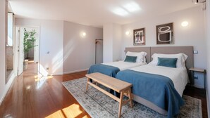 A modern bedroom with two beds, a bench, and a large window. - Feel Porto Ribeira Vintage Duplex (Oporto)