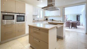 A modern kitchen with built-in ovens, a central island, and a dining area with wicker furniture. - #Luxury 4 Bed Villa, Heated Pool, Cinema, Gym, Sauna, Squash Court (La Cala)