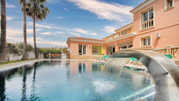A swimming pool with a water feature, surrounded by a building with balconies and a clear sky. - #Luxury 4 Bed Villa, Heated Pool, Cinema, Gym, Sauna, Squash Court (La Cala)