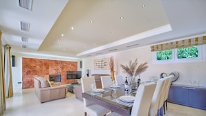 A modern dining area with a glass-top table, white chairs, and a sofa in the background. - #Luxury 4 Bed Villa, Heated Pool, Cinema, Gym, Sauna, Squash Court (La Cala)