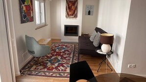 Una sala de estar moderna con un sofá, una silla, un tapete estampado, una chimenea y obras de arte en las paredes.