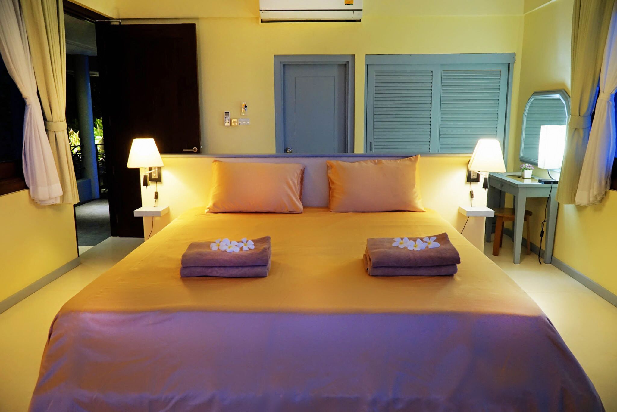 A double bed with two pillows, bedside lamps, a small table with a lamp, and a mirror.