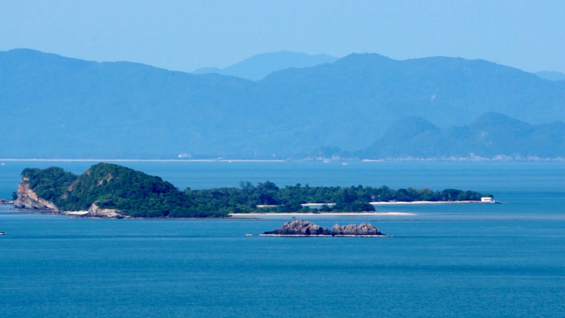 A coastal landscape with a large island, a smaller rocky outcrop, and distant mountains.