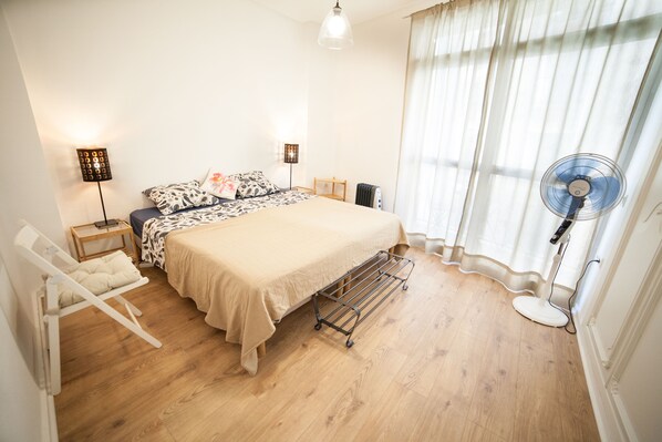 A bedroom with a bed, bedside lamps, a standing fan, a radiator, and a window with curtains. - Fantastic 160m² renovated house with Rooftop Terrace (Málaga)