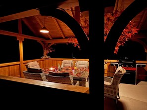 Un espacio al aire libre acogedor con mobiliario de mimbre, una mesa con velas y un tronco de árbol grande al frente.