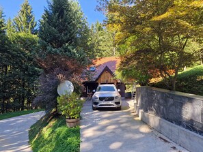 Une maison devant laquelle est garée une voiture, entourée d’arbres et d’un mur de pierres.