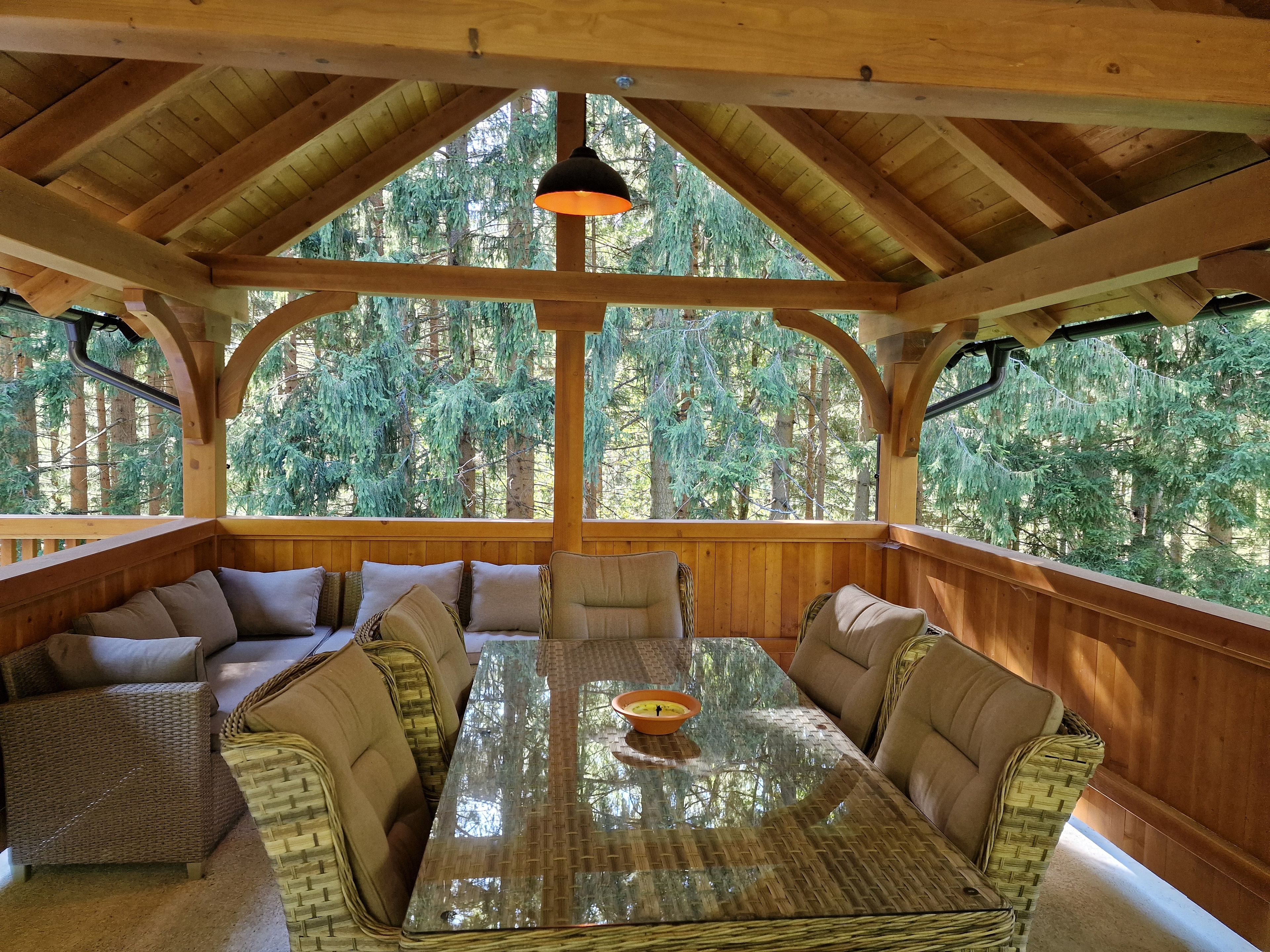A wooden interior with a glass-top table and wicker furniture, surrounded by a forest view.
