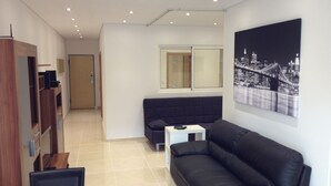 Un salon moderne avec un canapé en cuir noir, une petite table d’appoint blanche et un tableau représentant un paysage urbain accroché au mur.