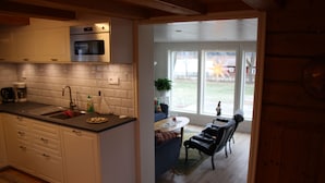 Una cocina con armarios blancos, microondas y fregadero. Hay una zona de comedor con mesa y sillas, y vistas al exterior.