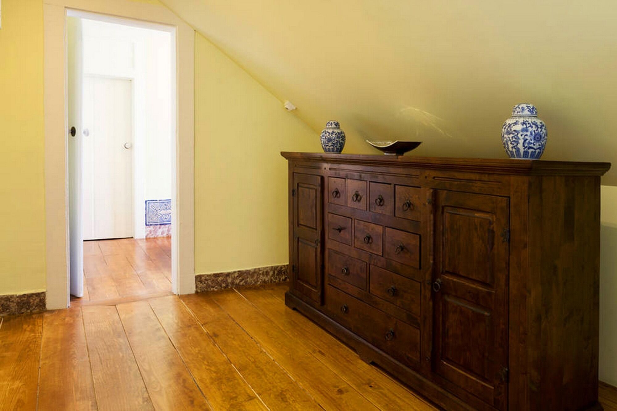 Ein Flur mit Holzboden, einem dunklen Holzschrank mit Schubladen und zwei blau-weißen, gemusterten Vasen darauf.