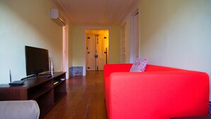 A room with a red sofa, a TV on a wooden stand, and a hallway leading to a door. - Apartment Baixa/Chiado view Castle (Lisboa)
