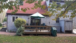 Una casa con un porche cubierto, una terraza de madera y un paraguas verde.