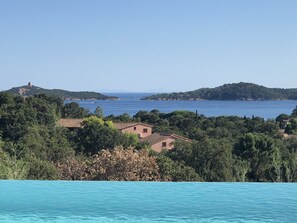 Vista costeira com céu azul límpido, um corpo de água e uma colina com uma torre.