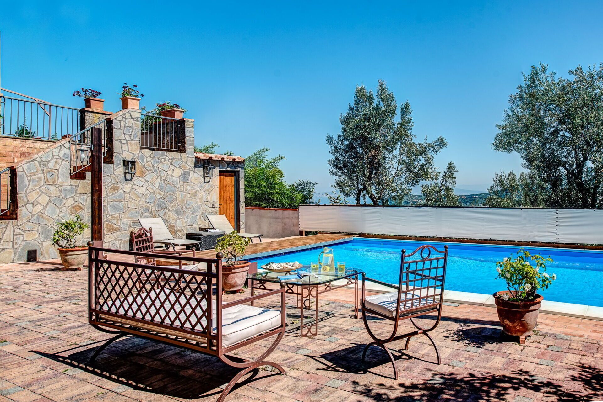 A poolside area with stone walls, lounge chairs, and a table with drinks.