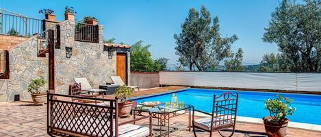 A poolside area with stone walls, lounge chairs, and a table with drinks.