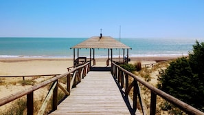 A wooden boardwalk leading to a beach with a wooden shelter at the end.