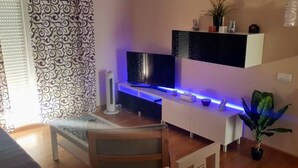 A modern living room with a flat-screen TV, a white console table, and a potted plant. - Excellent apartment in Rota, with pool, Wifi and garage (ROTA)