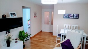 A living room with a TV, a dining table with chairs, a plant, and a door leading to another room. - Excellent apartment in Rota, with pool, Wifi and garage (ROTA)