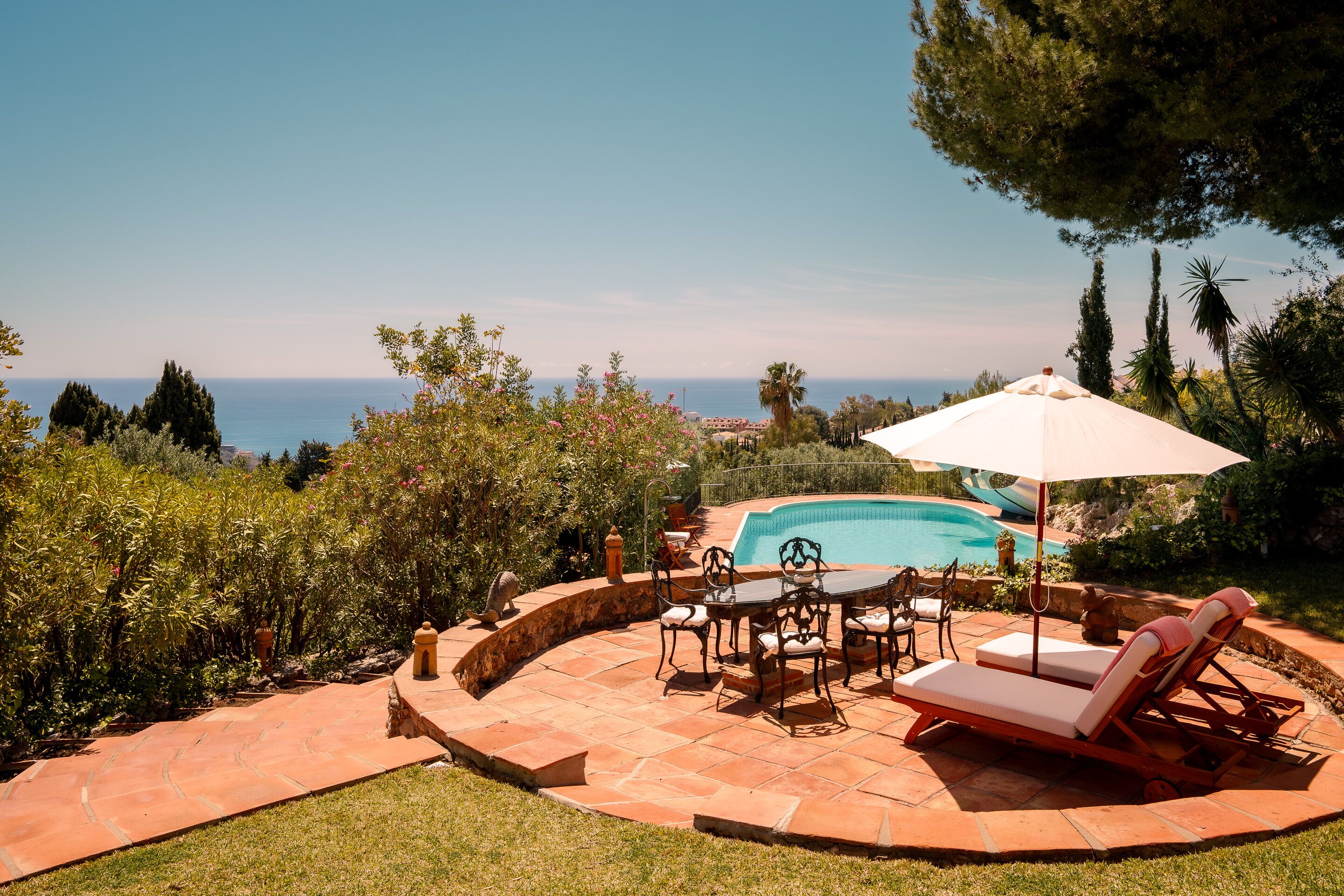 Un espace aménagé au bord de la piscine, avec une table et des chaises, une chaise longue et un grand parasol.