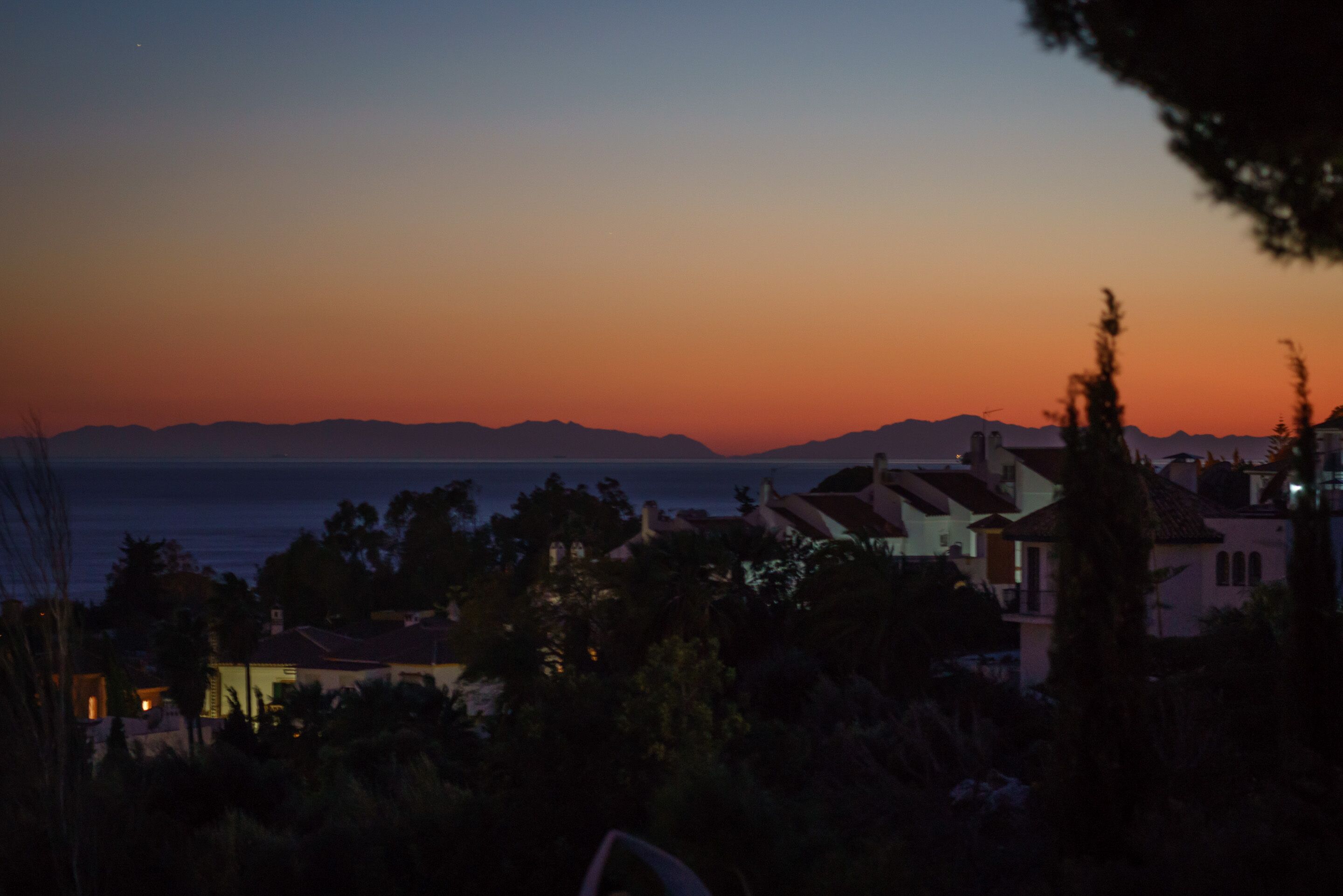 A coastal residential area with houses and a view of the sea during sunset.