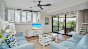 Een moderne woonkamer met een bank, salontafel, televisie en een balkon met buitenmeubels.