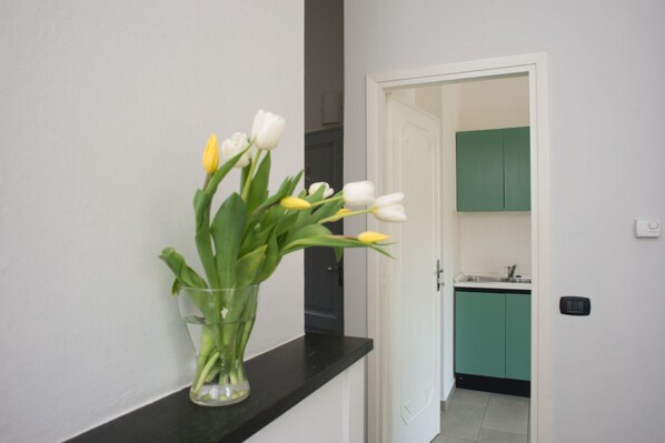 A hallway with a vase of tulips on a black countertop, leading to a kitchen with teal cabinets.