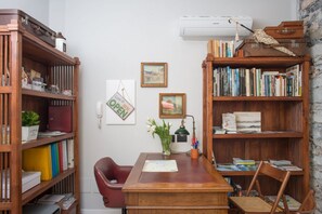 Una sala studio con una scrivania in legno, due librerie, una sedia rossa e un condizionatore d'aria a parete.