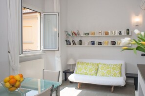 A modern room with a glass table, a white sofa, a bookshelf with books and mugs, and a window with curtains. - La Corte di Zizi-apartament Cernobbio: for couples and families (Cernobbio)