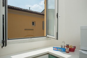 A bathroom with a window, a white sink, a bar of soap, a bottle of hand soap, and a basket of bread.
