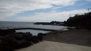 A coastal scene with a rocky shoreline, a concrete walkway, and a body of water. - Large 2 bedroom apartment (Açores)
