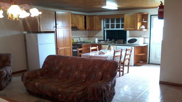 A living room with a sofa, a dining table with chairs, and a kitchen area with wooden cabinets and appliances. - Large 2 bedroom apartment (Açores)