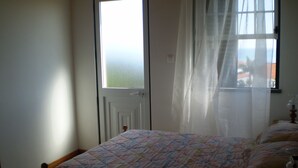 A bedroom with a bed, a window with sheer curtains, and a view of the outside. - Large 2 bedroom apartment (Açores)