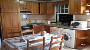 A compact kitchen with wooden cabinets, a stove, a microwave, and a washing machine. - Large 2 bedroom apartment (Açores)