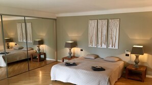 A bedroom with a large mirror, two bedside tables with lamps, a bed with a quilted cover, and a white fur rug on the floor.
