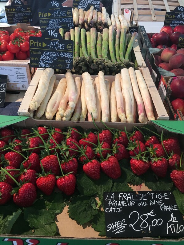 A market stall with fresh produce including asparagus, tomatoes, and strawberries.