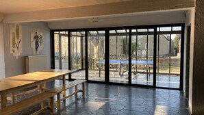 Una habitación amplia con una mesa grande y bancos, ventanas grandes y vistas al exterior.