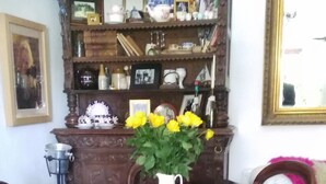 Una sala da pranzo con un tavolo e sedie in legno, un vaso con fiori gialli e una mensola con diversi oggetti.